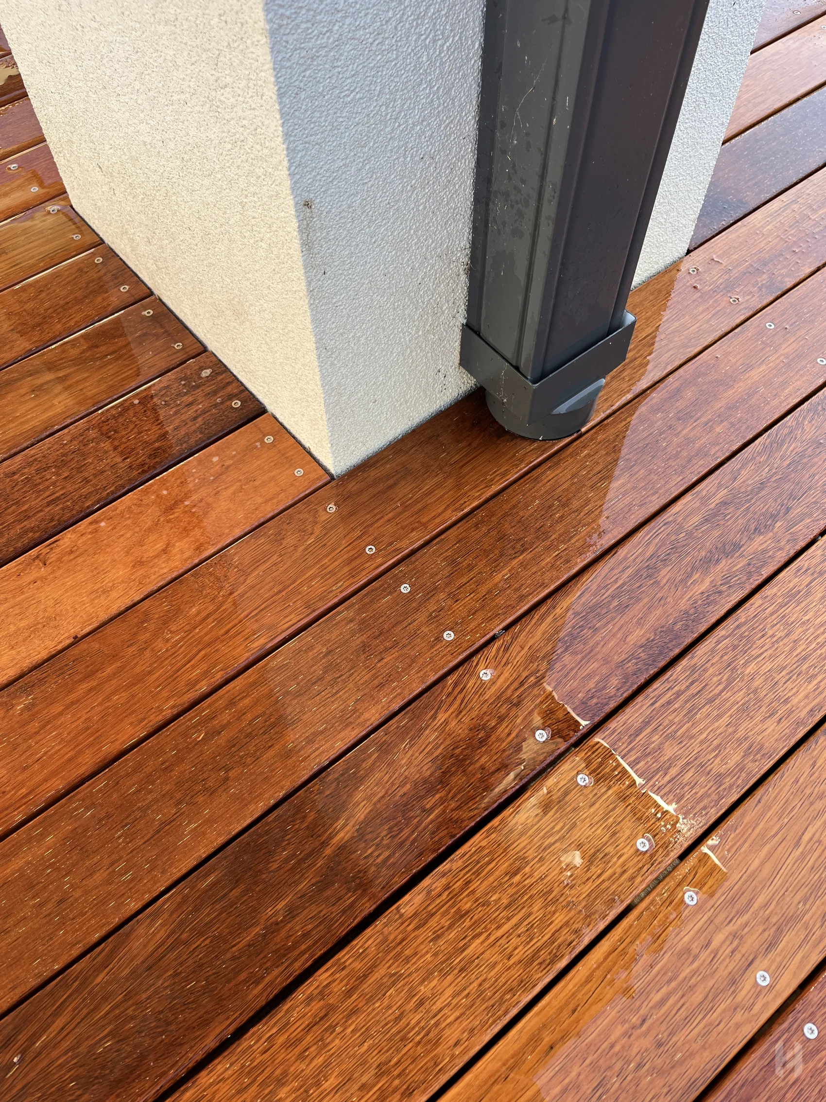 Timber decking detail around a black post with exposed fixings and natural board grain